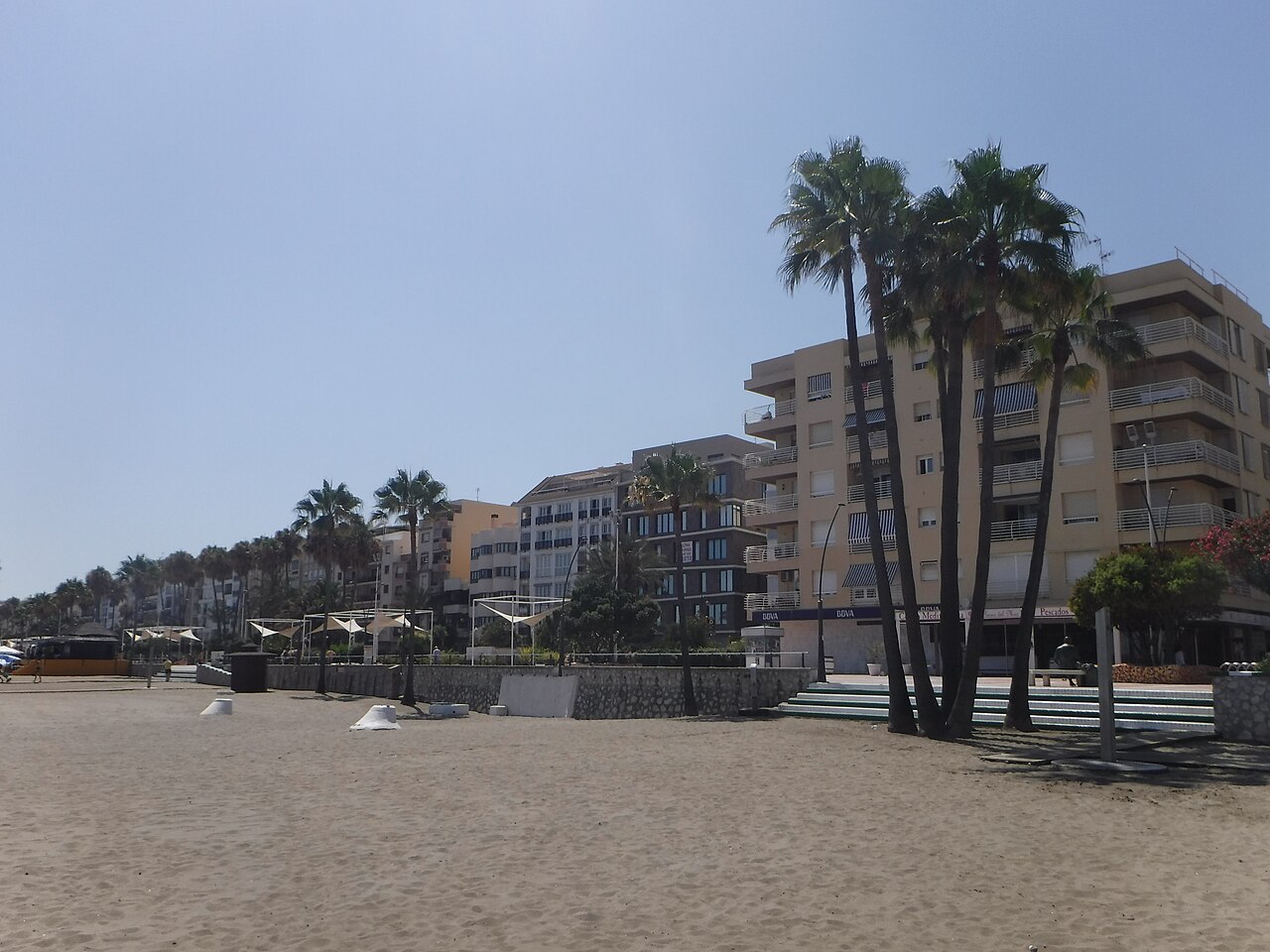 Amplia playa de arena en Playa de la Rada en Estepona con palmeras y bloques de apartamentos detrás